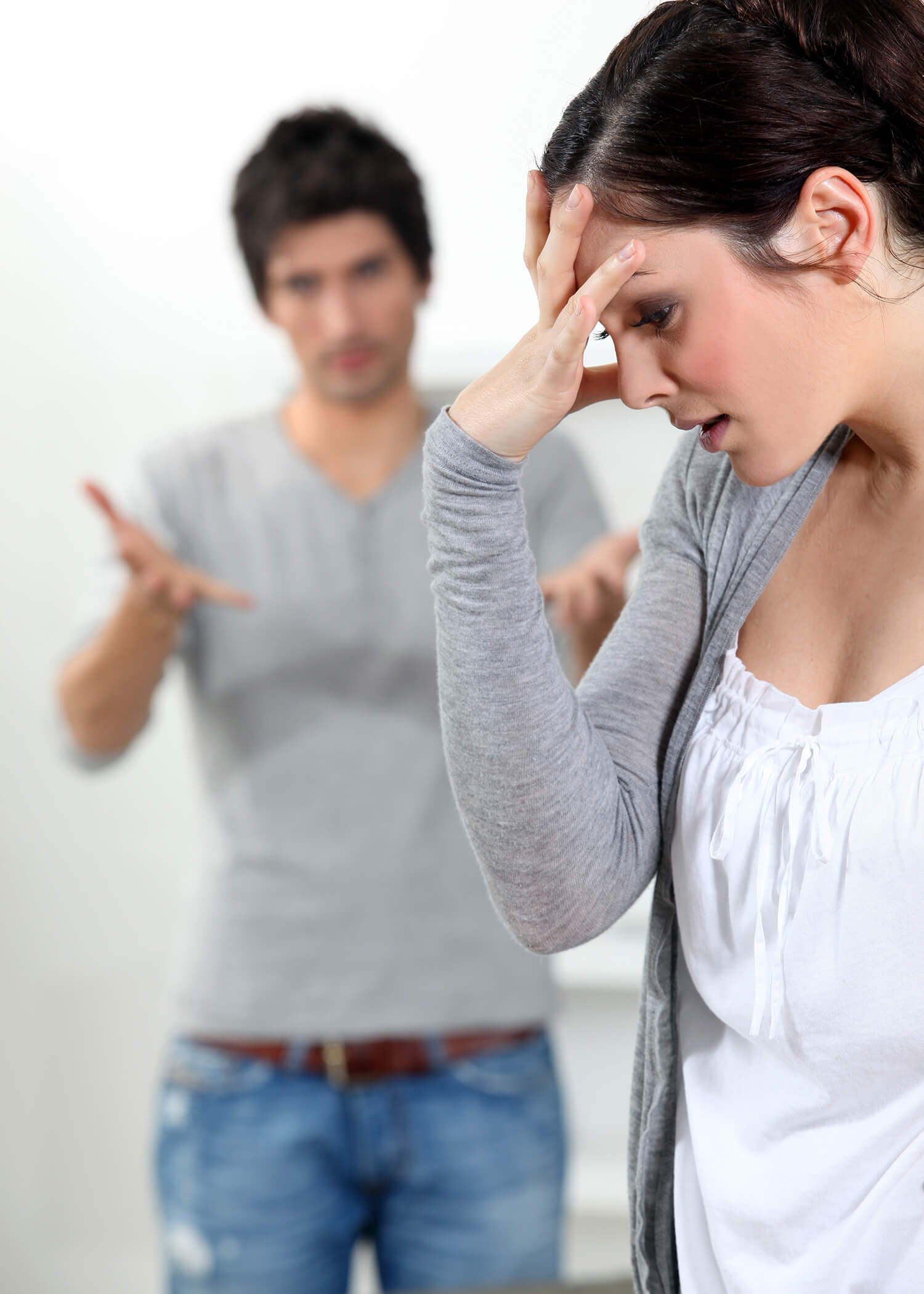 Image of a woman with her hand held to her forehead while a man in the background holds two hands out to her. The woman represents individuals who could benefit from searching for "DBT program in Los Angeles, CA" and working with a DBT therapist in Torrance, CA. 90274 | 90275