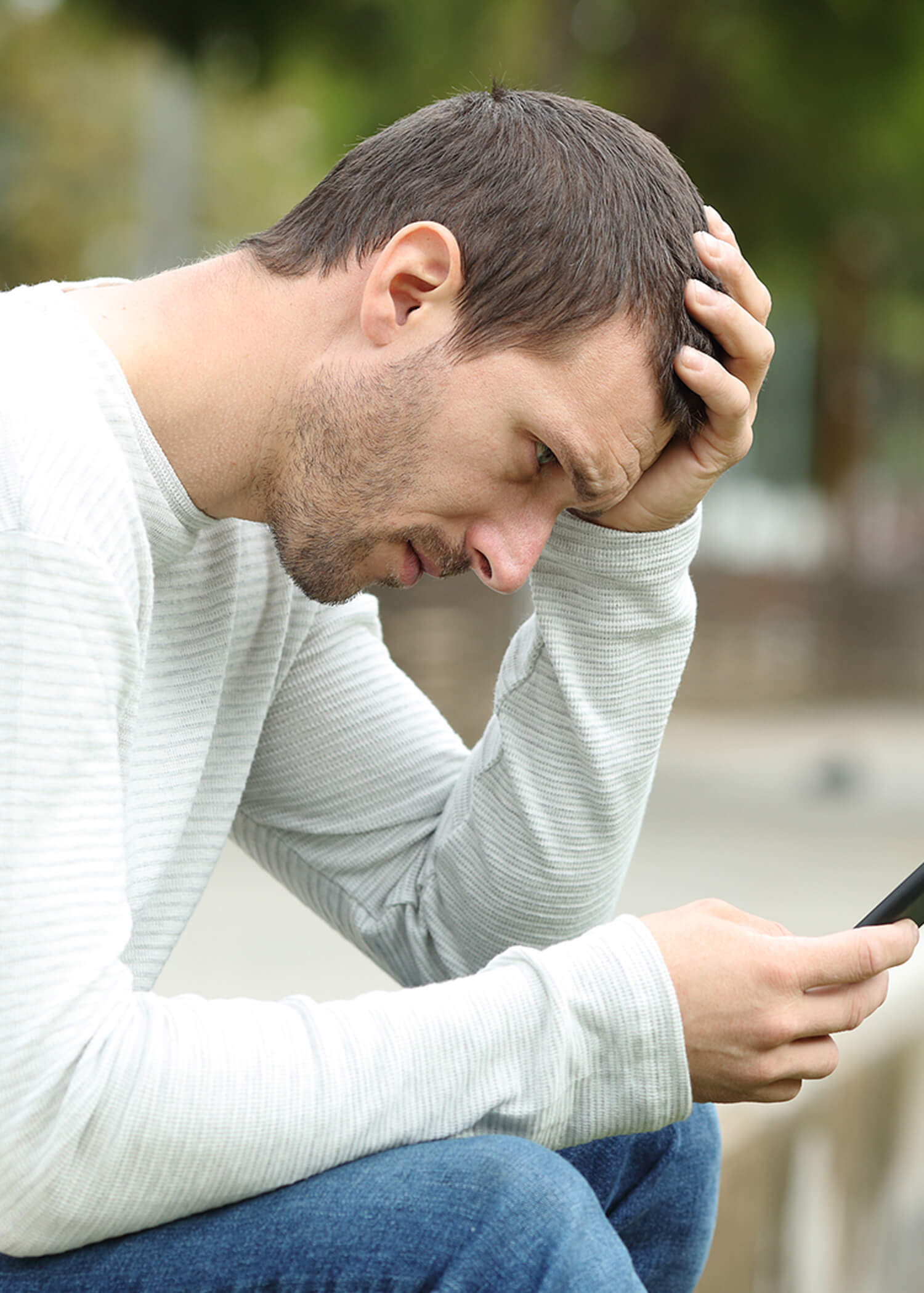 Image of a man wearing a white sweater looking at his phone with a frustrated look on his face. This photo depicts what a person having suicidal thoughts may look like. Those experiencing this can get help in therapy for suicidal thoughts in Los Angeles, CA with a DBT therapist. | 90274 | 90275