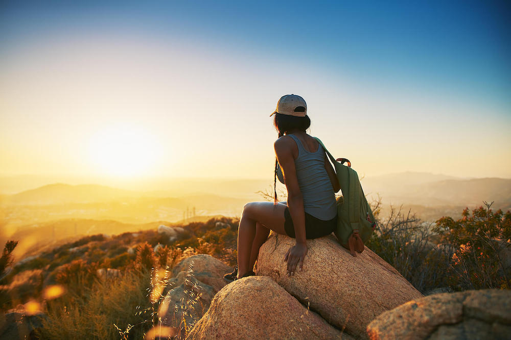 Image of a woman sitting on a rock looking at the sunset over a desert. Do you struggle with stress? Learn how to destress with the help of DBT therapy in Las Vegas, NV.