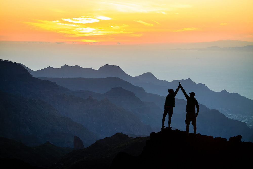 Image of two people high-fiving on top of a cliff during sunset. Learn to destress and manage your emotions with the help of DBT therapy in Las Vegas, NV.