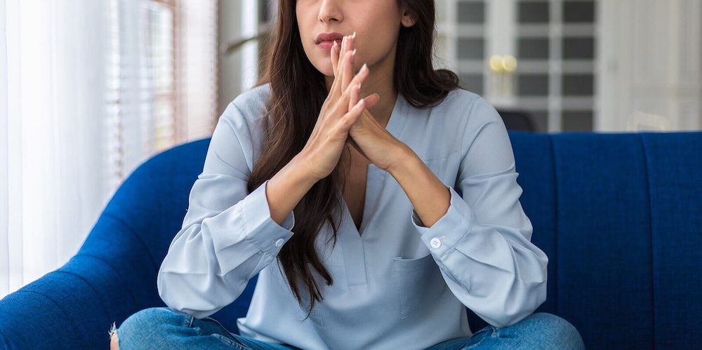 Image of an anxious woman sitting on a couch with her hands clasped in front of her. If you struggle with anxiety symptoms, learn how EMDR therapy in Las Vegas, NV can help alleviate your symptoms.