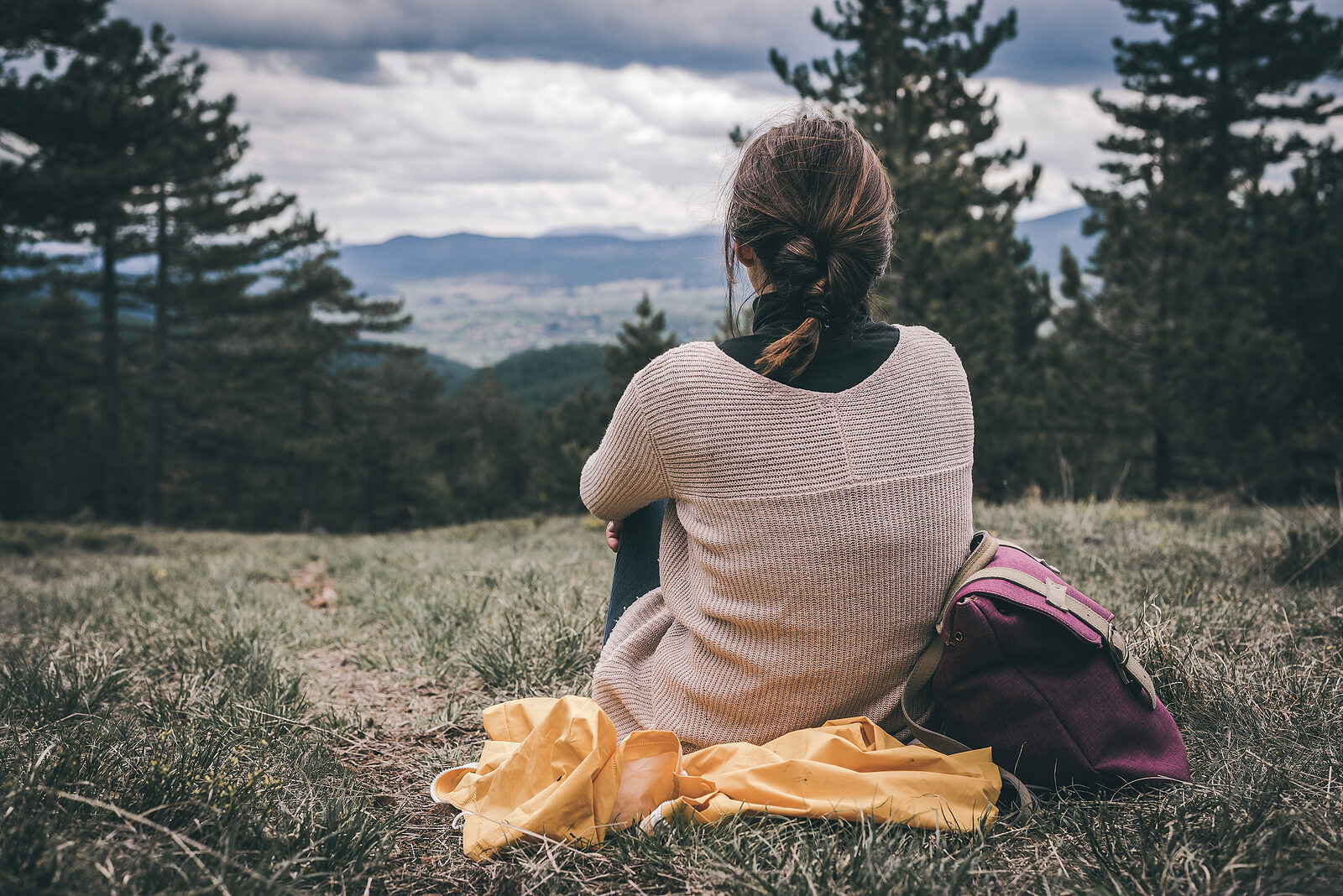 Image of a woman sitting on the ground on a cloudy day looking out at mountains. If you struggle with depression, learn how EMDR therapy in Las Vegas, NV can help you cope with your symptoms in healthy ways.