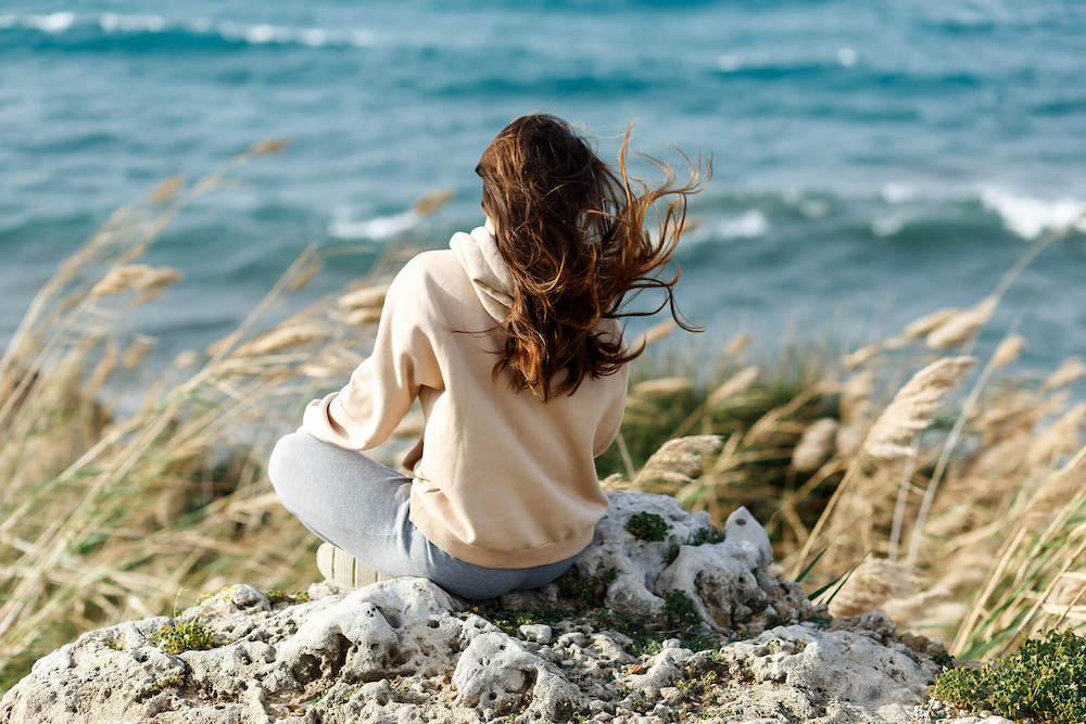 Image of a woman sitting on a rock near the ocean with the wind blowing through her hair on a sunny day. Discover how EMDR Therapy in Las Vegas, NV can help you work to overcome your symptoms of anxiety, depression, and more in a rapid way.