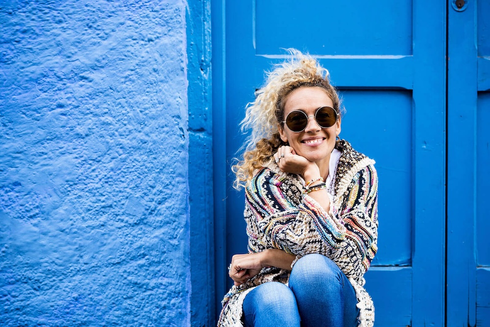 Image of a smiling woman wearing sunglasses sitting on the doorstep of a blue building. Discover the power of EMDR therapy in Las Vegas, NV and how it can help you cope with your symptoms in healthy ways.