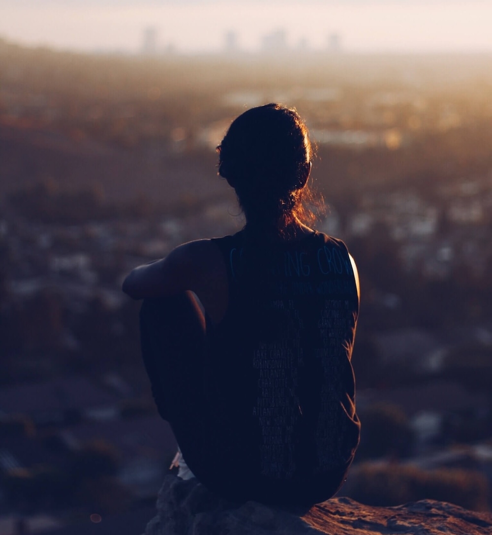 Image of a woman sitting on a rock overlooking a city. If you struggle with DID symptoms, learn how an EMDR therapist in Las Vegas, NV can help you cope and manage them in effective ways.