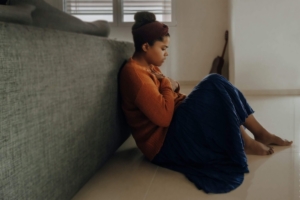 Image of a woman sitting on the floor leaning against a couch holding her hand to her chest. Discover how you can fight your anxiety symptoms with the help of EMDR therapy in Las Vegas, NV.