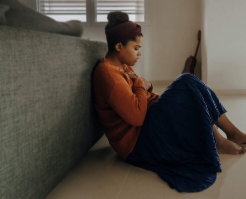 Image of a woman sitting on the floor leaning against a couch holding her hand to her chest. Discover how you can fight your anxiety symptoms with the help of EMDR therapy in Las Vegas, NV.