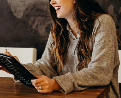 Image of a smiling young woman sitting at a table holding a laptop. Uncover how you can begin healing from trauma with the help of EMDR therapy in Las Vegas, NV.