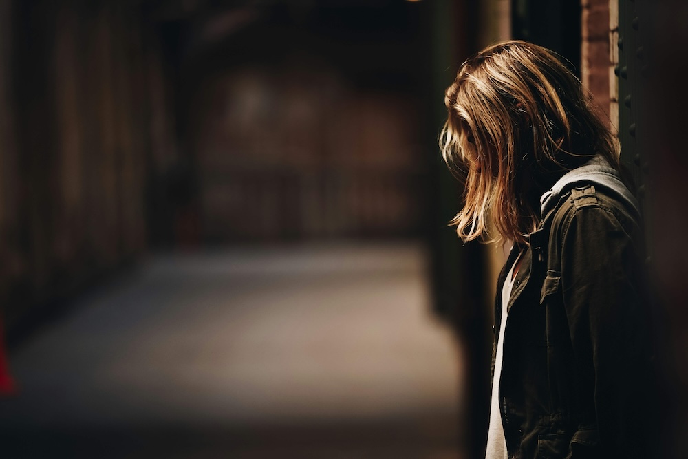 Image of a woman leaning against a brick building looking down in sadness. If trauma is causing you stress, learn how EMDR therapy in Las Vegas, NV can help.