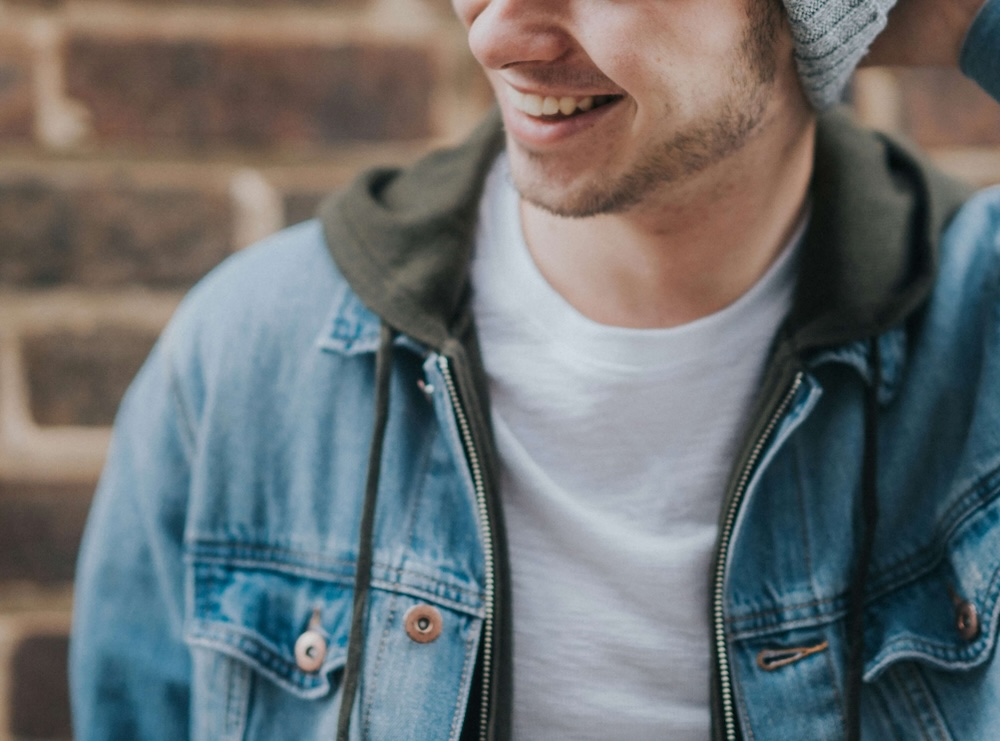 Image of a smiling young man wearing a jean jacket standing outside near a brick wall. Overcome your depression symptoms with the help of EMDR therapy in Las Vegas, NV.