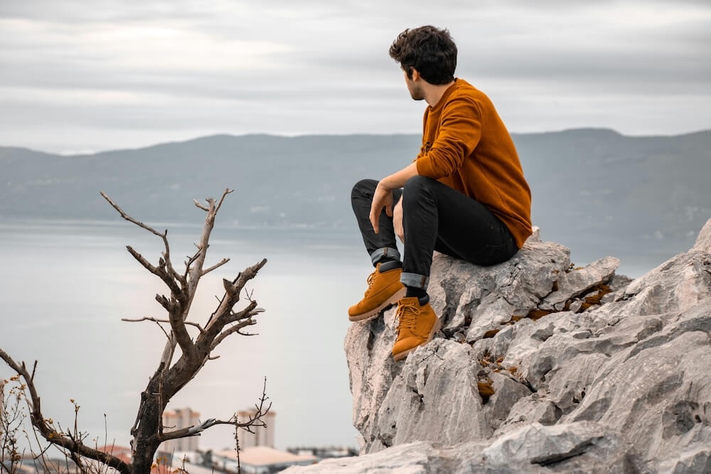 Image of a man sitting on top of a rock on a hill looking out over a lake during the day. Uncover new ways to manage you recent trauma with the help of EMDR therapy in Las Vegas, NV.