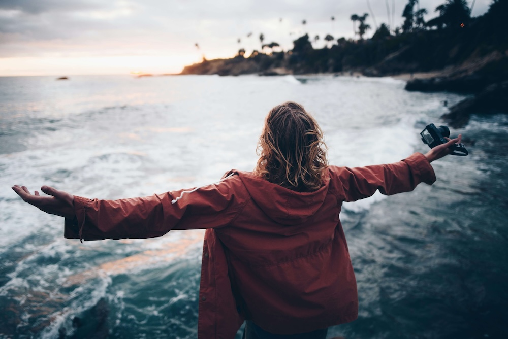 Image of a woman standing by the ocean during sunset with her arms spread out. Learn to break free from your trauma with EMDR therapy in Las Vegas, NV.