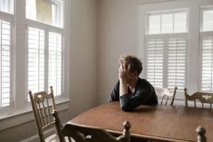 A man sitting at a wooden table with his head in his hand, looking distressed. A DBT therapist in Las Vegas can help you process emotions and regain balance through dialectical behavior therapy in Las Vegas.