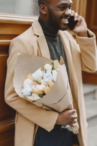 Shows a man smiling, talking on the phone, and holding white tulips. Represents how dbt las vegas and how a dbt therapist in las vegas can help you separate your needs and wants from your partner's.