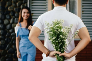 Shows a man in a white shirt holding white flowers behind his back in front of his wife. Represents how debt therapy in Las Vegas and a dbt therapist in Las Vegas can help you in your relationship.