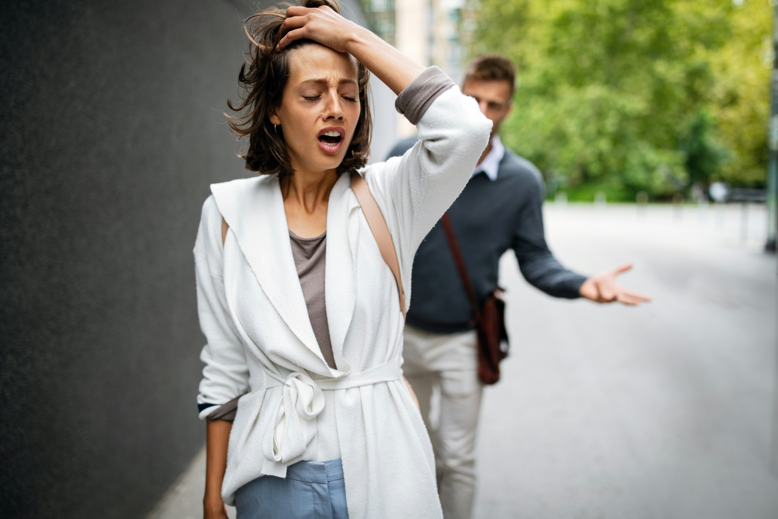 A distressed woman holding her head while a man argues in the background, representing emotional dysregulation and conflict in ADHD.