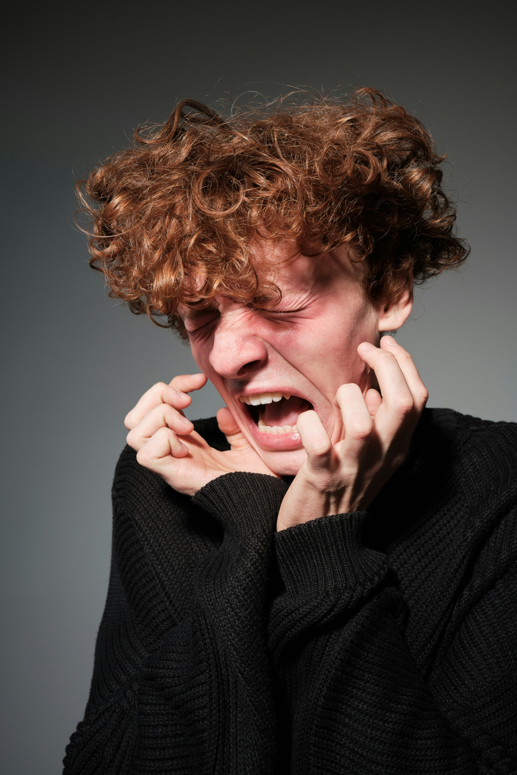 A young person with curly hair gripping their face in distress, showing the intensity of emotional dysregulation.