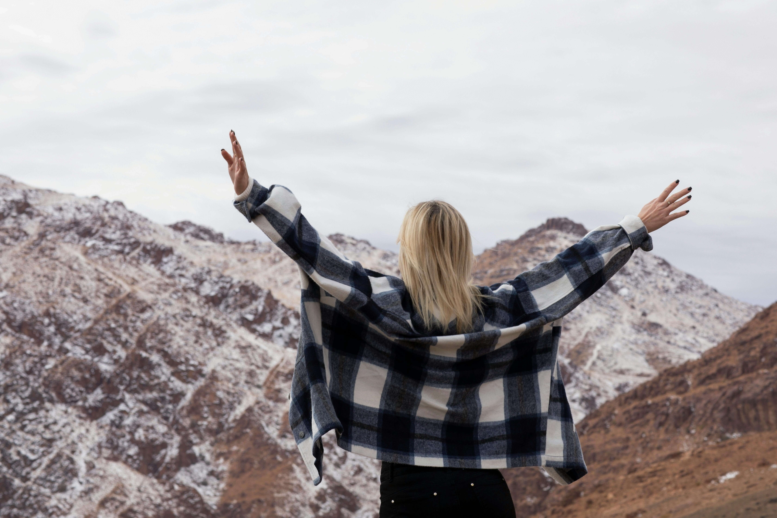 Photo of a woman in a plaid shirt standing with arms raised toward the snowy mountains, celebrating victory. Want to learn DBT skills to build resilience against emotional storms? A DBT therapist in Las Vegas, NV, can help you strengthen your coping strategies and emotional balance.