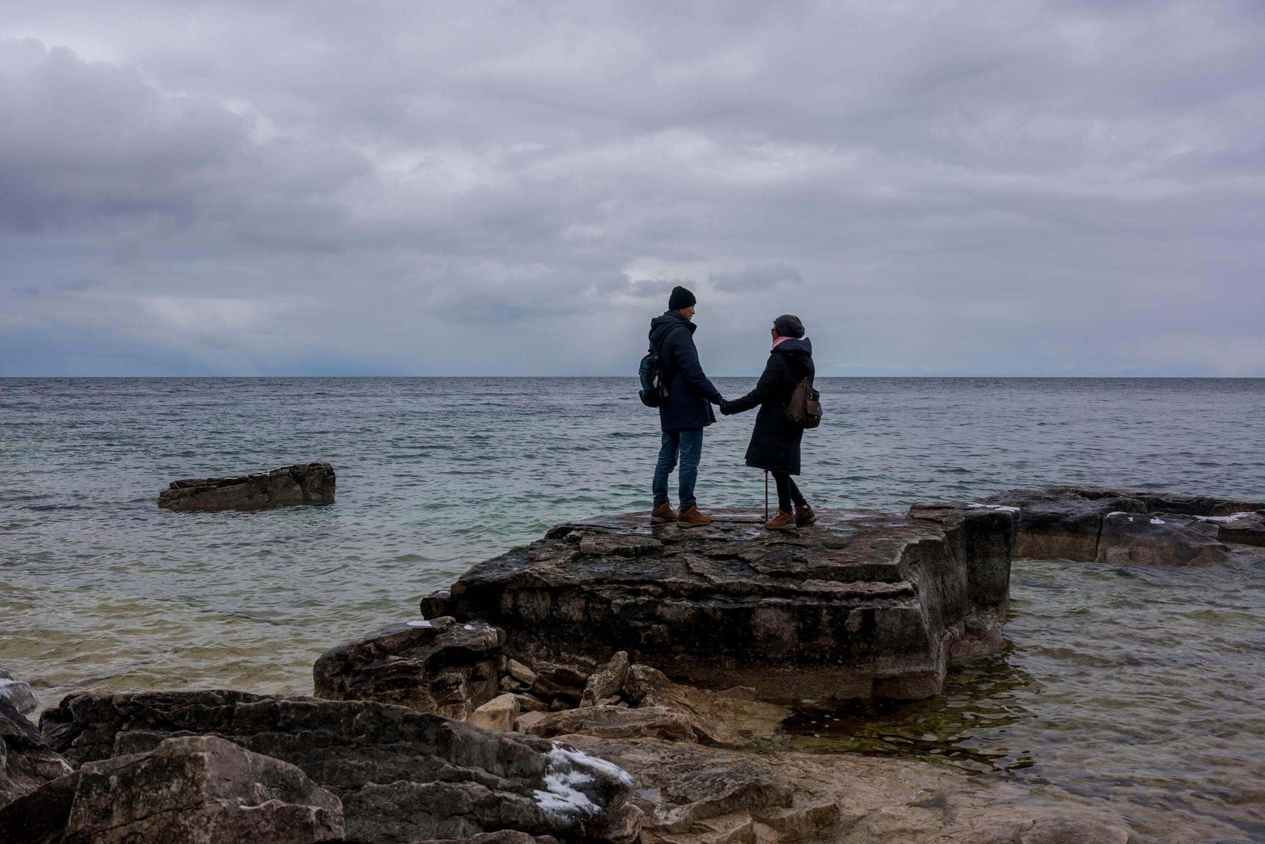 A couple stands on rocks by the sea, holding hands under a cloudy sky. DBT therapy fosters mindful communication and emotional balance, while EMDR therapy in Las Vegas, NV, supports healing from trauma within safe relationships.
