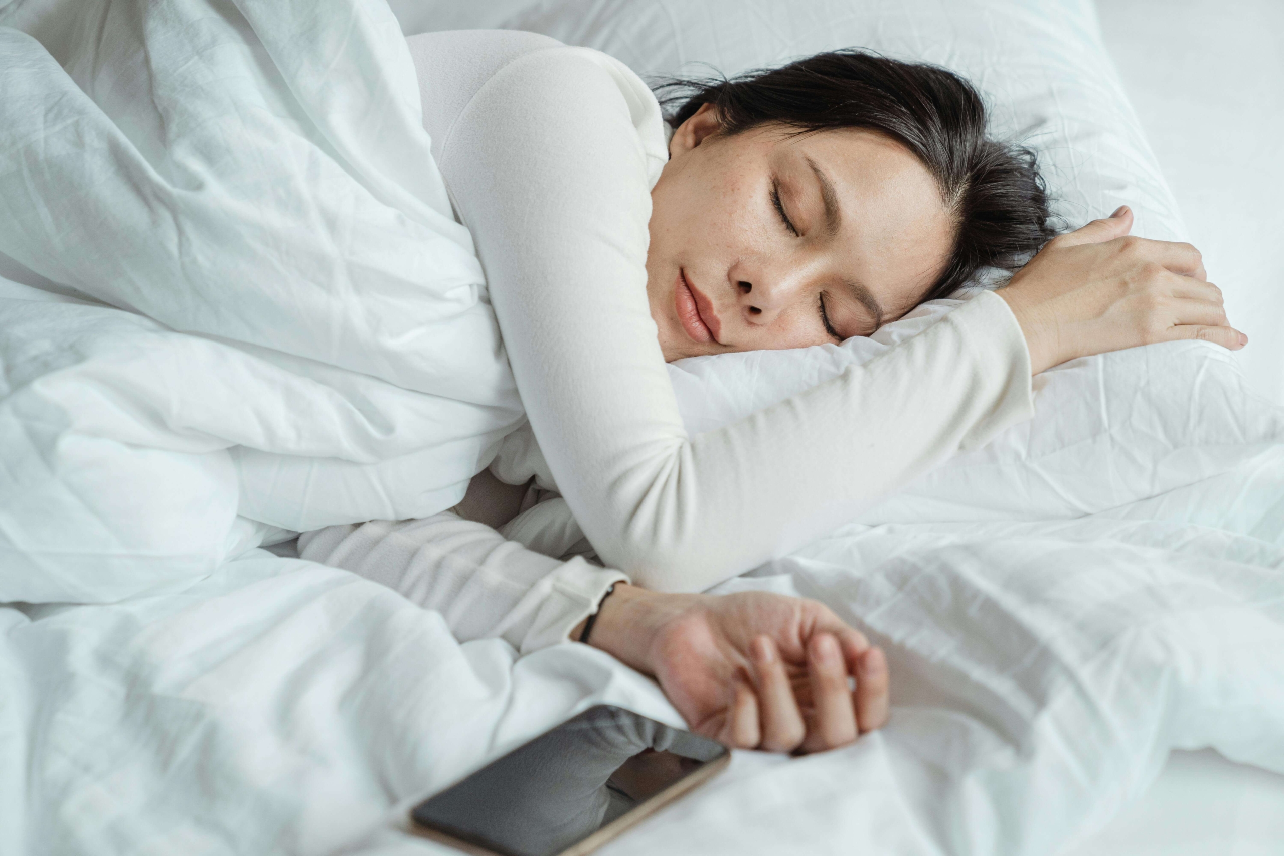 A woman rests peacefully in bed with her phone nearby. Practicing DBT skills, like adequate sleep, supports emotional balance. Through DBT therapy in Las Vegas, individuals learn how physical self-care helps regulate emotions and prevent emotional burnout.