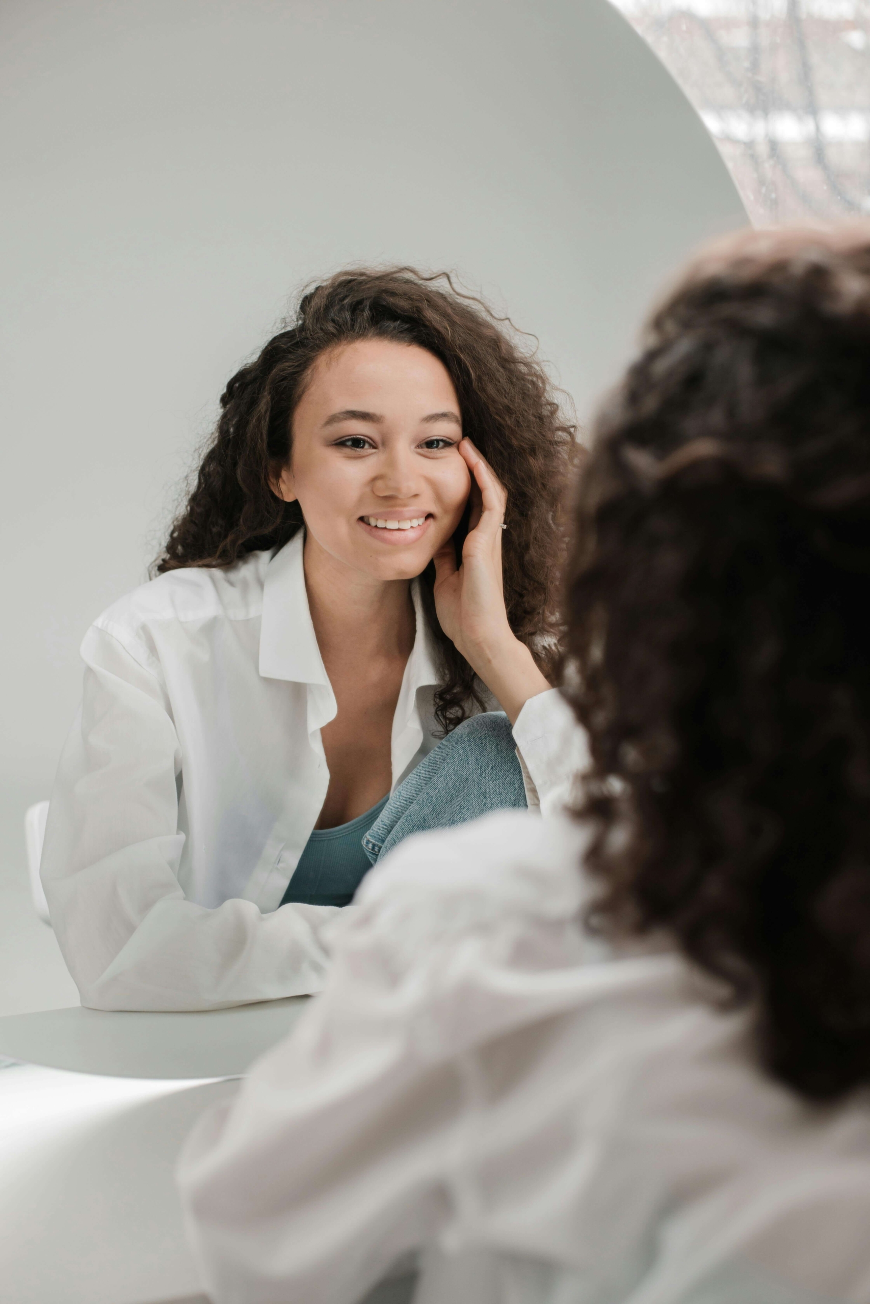 Photo of a smiling woman sitting and looking at herself in the mirror with confidence. Do you want to build DBT skills and learn emotional regulation for a calmer life? DBT therapy in Las Vegas, NV, can help you strengthen self-mastery and inner peace.