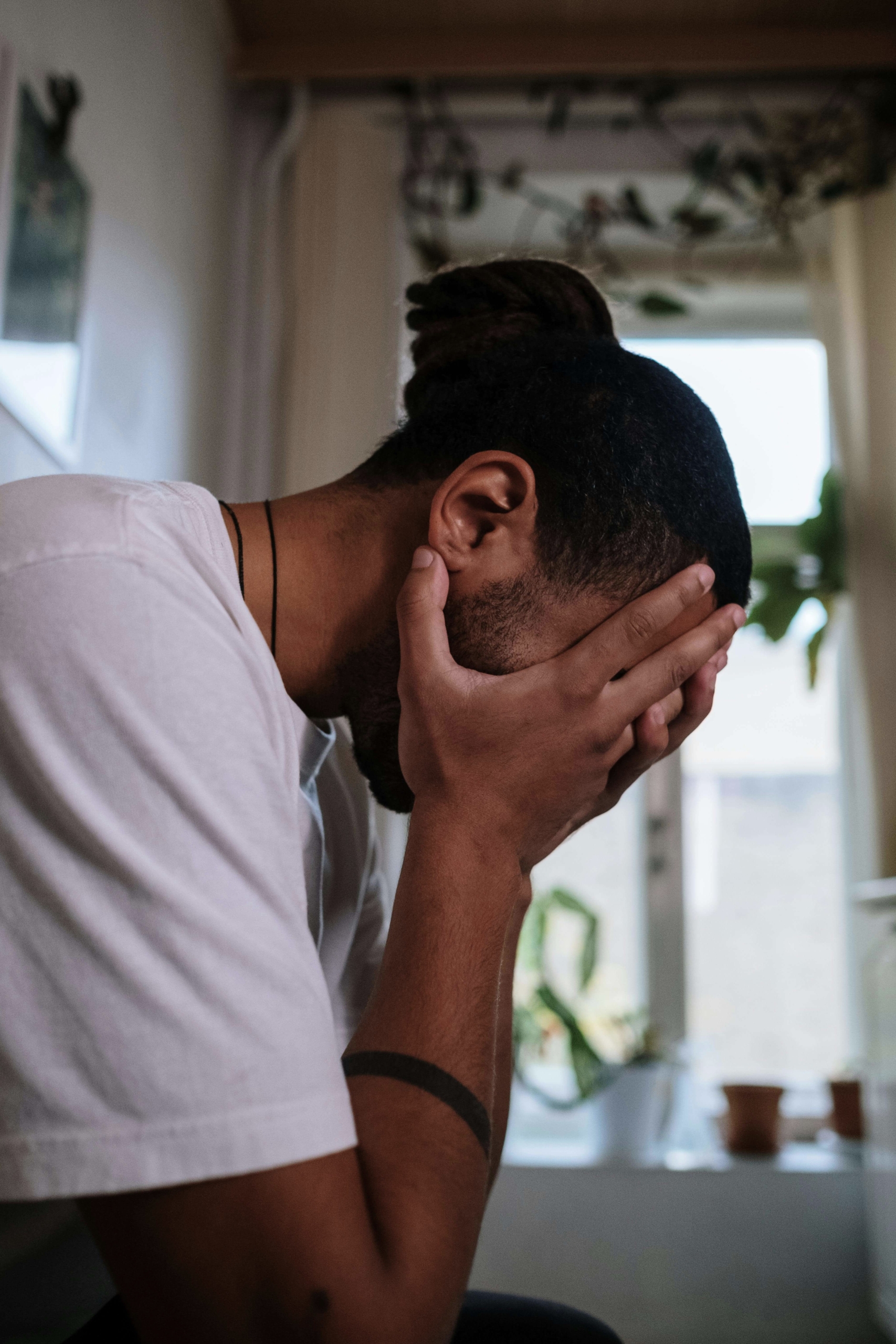 A man sits indoors with his face buried in his hands, showing deep emotional strain and fatigue. Are you searching for therapy for men that can help you settle silent overwhelm? An Online DBT therapist in Torrance, CA, helps men manage tough emotions.