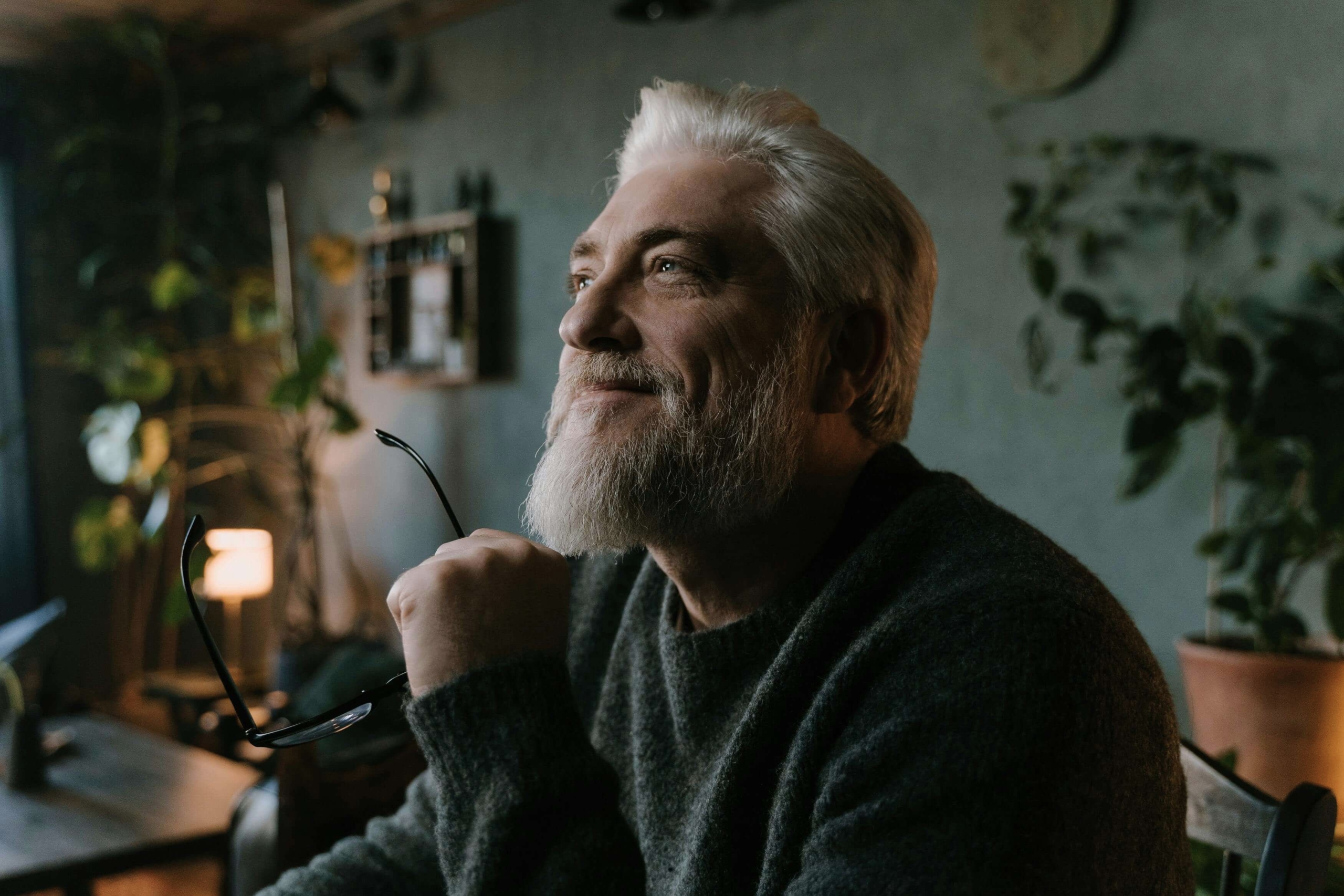 An older man with a gray beard gazes upward with a calm smile in a softly lit room. Wondering if men’s therapy could help ease your quiet struggles? Online DBT therapy in Las Vegas, NV, guides men toward steadier emotions during tough moments.