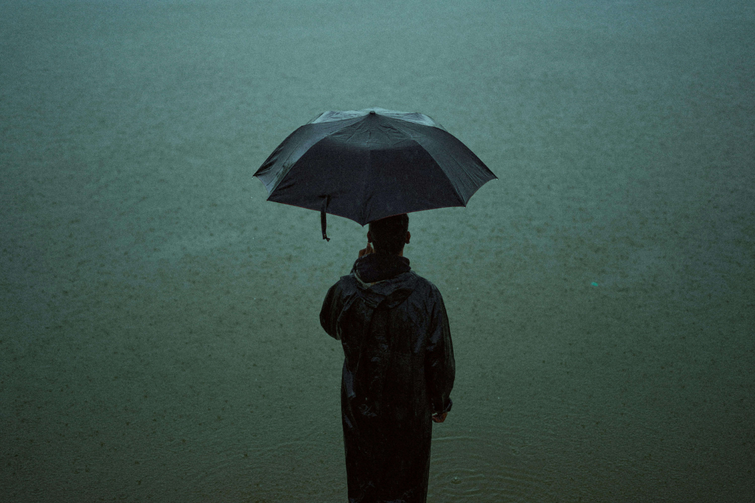 A person holding an umbrella stands alone in the rain, representing calm within emotional storms. Mindfulness helps people observe their current emotion with compassion. Online DBT therapy in Las Vegas, NV, offers tools to stay balanced.